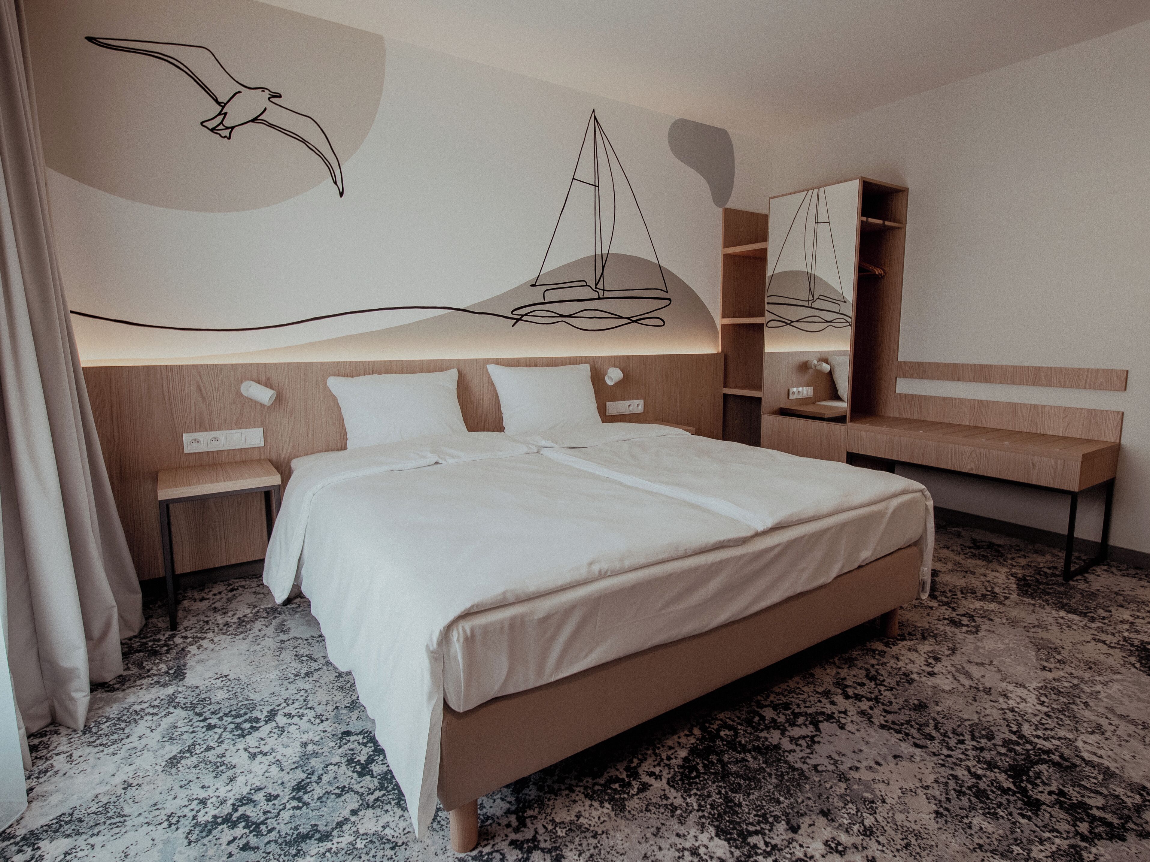 Una habitación de hotel moderna con una cama grande, cabecera de madera, un banco integrado y un estante fijado a la pared.