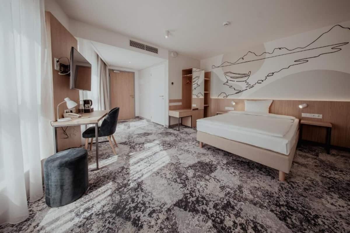 A modern hotel room with a large bed, a desk with a chair, a flat-screen TV, and a large abstract wall mural.