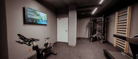 A gym with an exercise bike, a wall-mounted TV, and a weightlifting station.