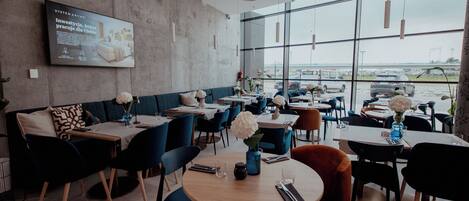 Un restaurante moderno con pared de concreto, sillas azul y naranja, y mesas con manteles blancos.