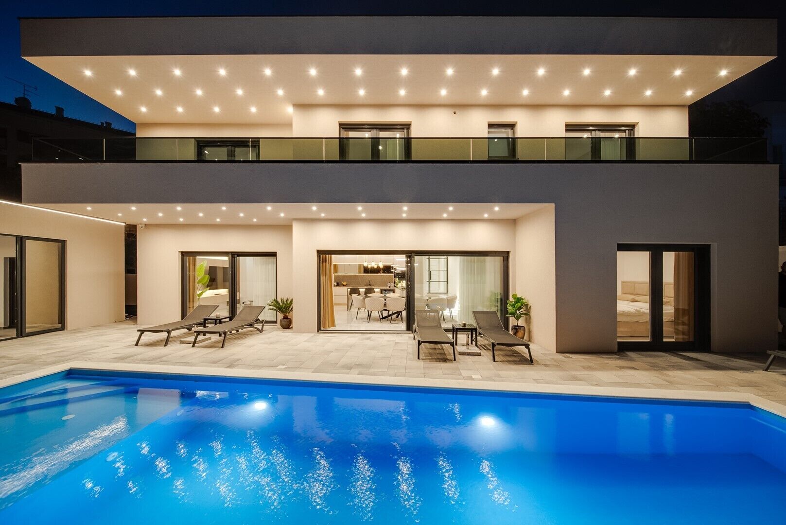 A modern two-story house with a swimming pool, outdoor seating, and a dining area.