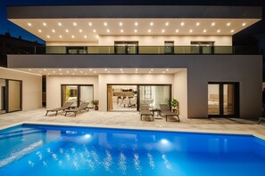 Ett modernt hus i två våningar med en swimmingpool, en uteplats och en matplats.