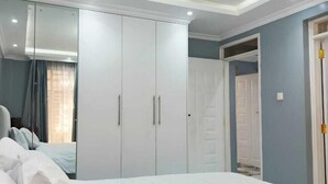 A bedroom with a large bed, white wardrobe, and a ceiling light fixture. - Lux Suites Grandville Apartments (Nairobi)