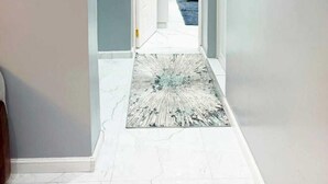A hallway with a marble floor, a white door at the end, and a blue rug leading to a room with a white dresser. - Lux Suites Grandville Apartments (Nairobi)