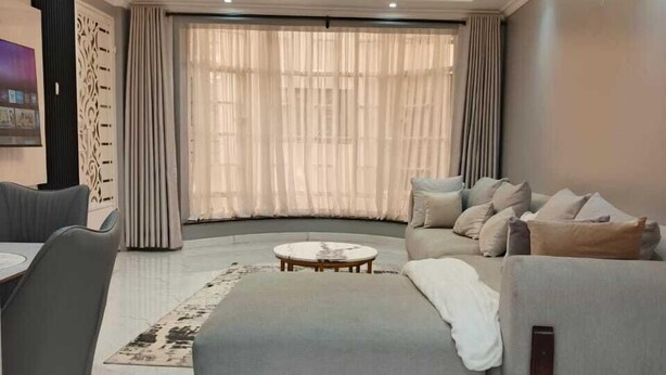 A modern living room with a sofa, ottoman, and a round coffee table. - Lux Suites Grandville Apartments (Nairobi)