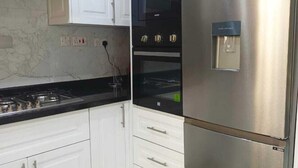 A modern kitchen with white cabinets, a stainless steel refrigerator, a black oven, and a gas stove. - Lux Suites Grandville Apartments (Nairobi)