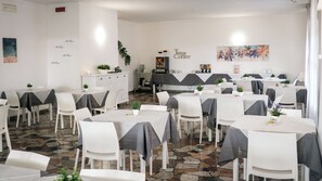 A restaurant with multiple tables and chairs, a coffee station, and a mural on the wall. - Hotel Fattori (Cesenatico)