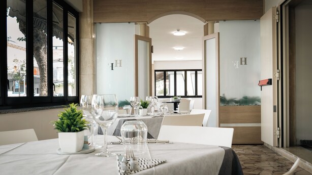 A dining area with tables set for two, featuring clear glassware and white tablecloths. - Hotel Fattori (Cesenatico)