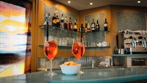 A bar area with two glasses of a red beverage, a bowl of snacks, and shelves with various bottles. - Hotel Fattori (Cesenatico)