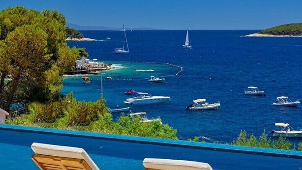 Zona de piscina con dos sillas reclinables de madera y vista al mar con barcos.