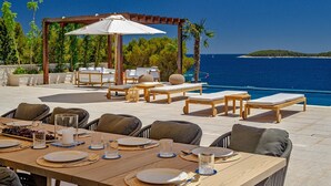 Un área de comedor al aire libre con pérgola, sillones de descanso y vista a la piscina.