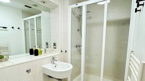 Uma casa de banho moderna com uma pia branca, espelho e cabine de duche em vidro.