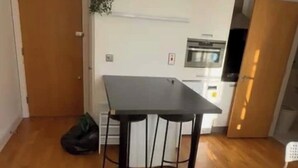 Uma cozinha compacta com bancada escura, uma geladeira pequena e um armário branco.