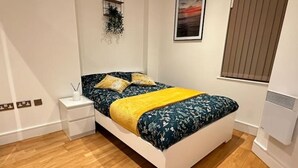 Quarto com cama, mesa de cabeceira e prateleira na parede.