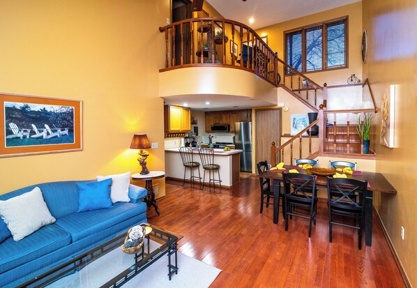 A spacious living area with a blue sofa, wooden dining table, and a kitchen in the background.