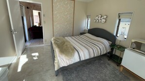 A bedroom with a bed, bedside table, lamp, and a window with blinds.