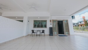 A spacious indoor area with a tiled floor, a ceiling fan, a table with chairs, a window with bars, and a door leading outside. - kings Pine Residences HomeStay 3-bedroom house with AC and WiFi in Ranau 14 (Ranau)