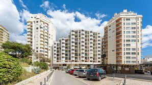 Un immeuble d’appartements moderne doté de nombreux balcons, d’un espace de stationnement avec des voitures et d’un ciel dégagé.