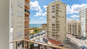 Un immeuble de grande hauteur doté de nombreux balcons, donnant sur une zone côtière où l’on aperçoit des voitures garées et une plage en arrière-plan.