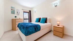 Une chambre à coucher avec un lit, une table de chevet, une commode et une fenêtre avec des rideaux.