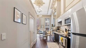 A modern kitchen with stainless steel appliances, a dining area with a chandelier, and a hallway leading to a living space.