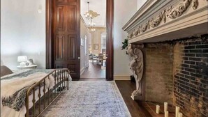 A room with a bed, a fireplace, a door leading to another room, and a patterned rug.