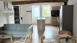 Un vaste espace de vie comprenant un canapé, des fauteuils en osier, une table à manger pour quatre personnes et, au fond, une cuisine.