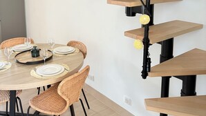 Un coin repas agrémenté d’un escalier en colimaçon, de chaises en osier et d’une table ronde dressée pour six personnes.