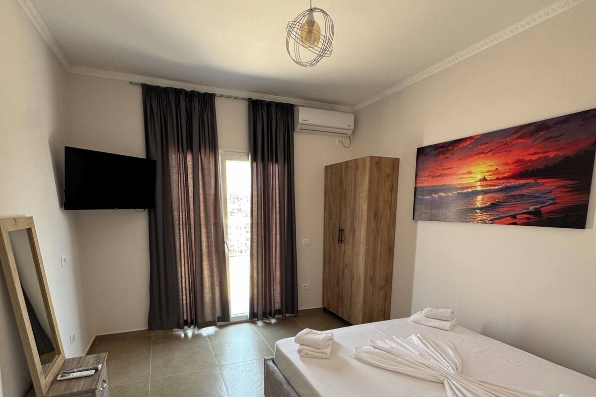 A hotel room with a bed, a painting, a television, and a wardrobe.