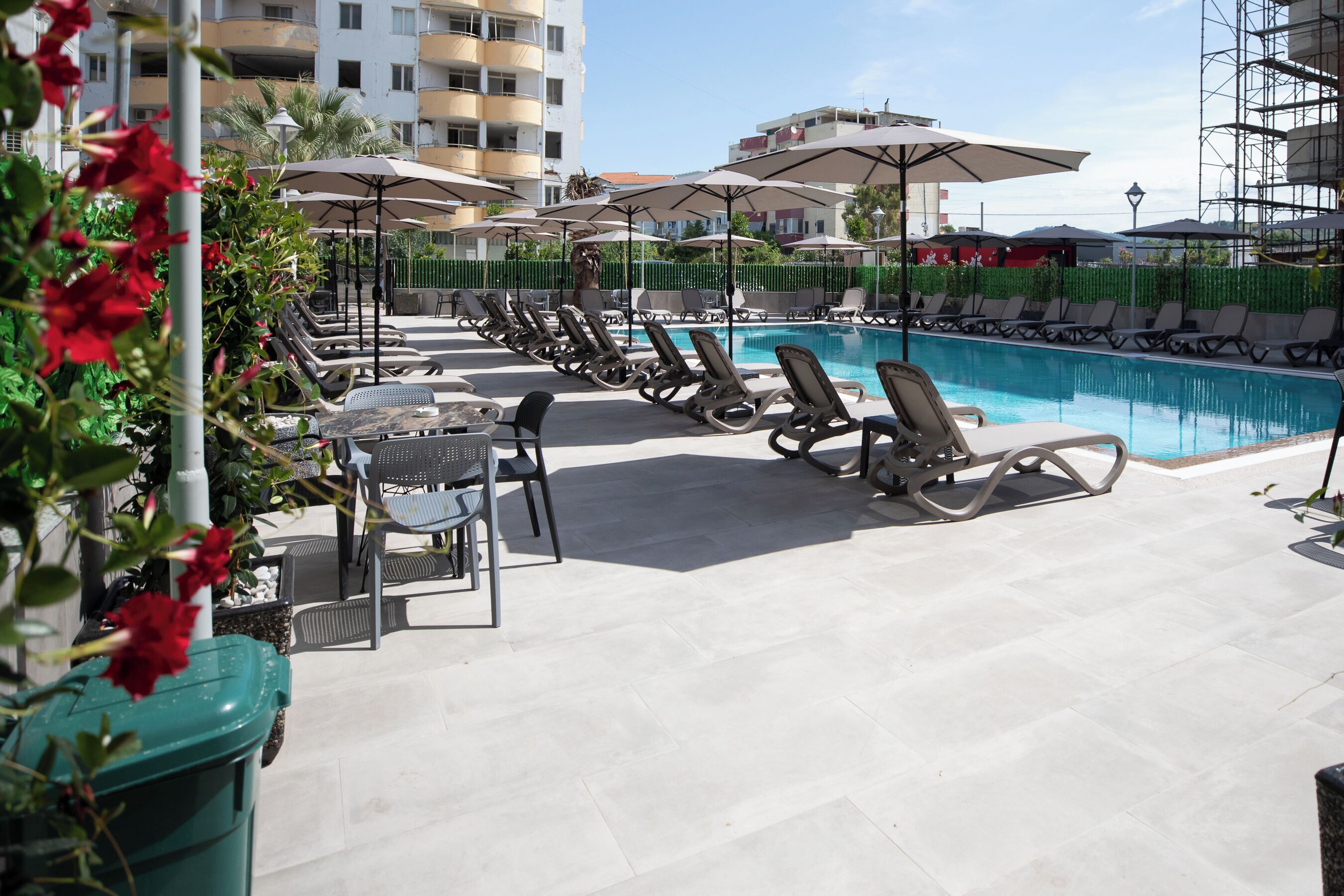 A poolside area with lounge chairs and umbrellas, a clear blue pool, and a building in the background.