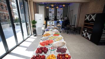 Una mesa de buffet con diversas frutas y aperitivos, un refrigerador y una zona de bar con estantes llenos de botellas.