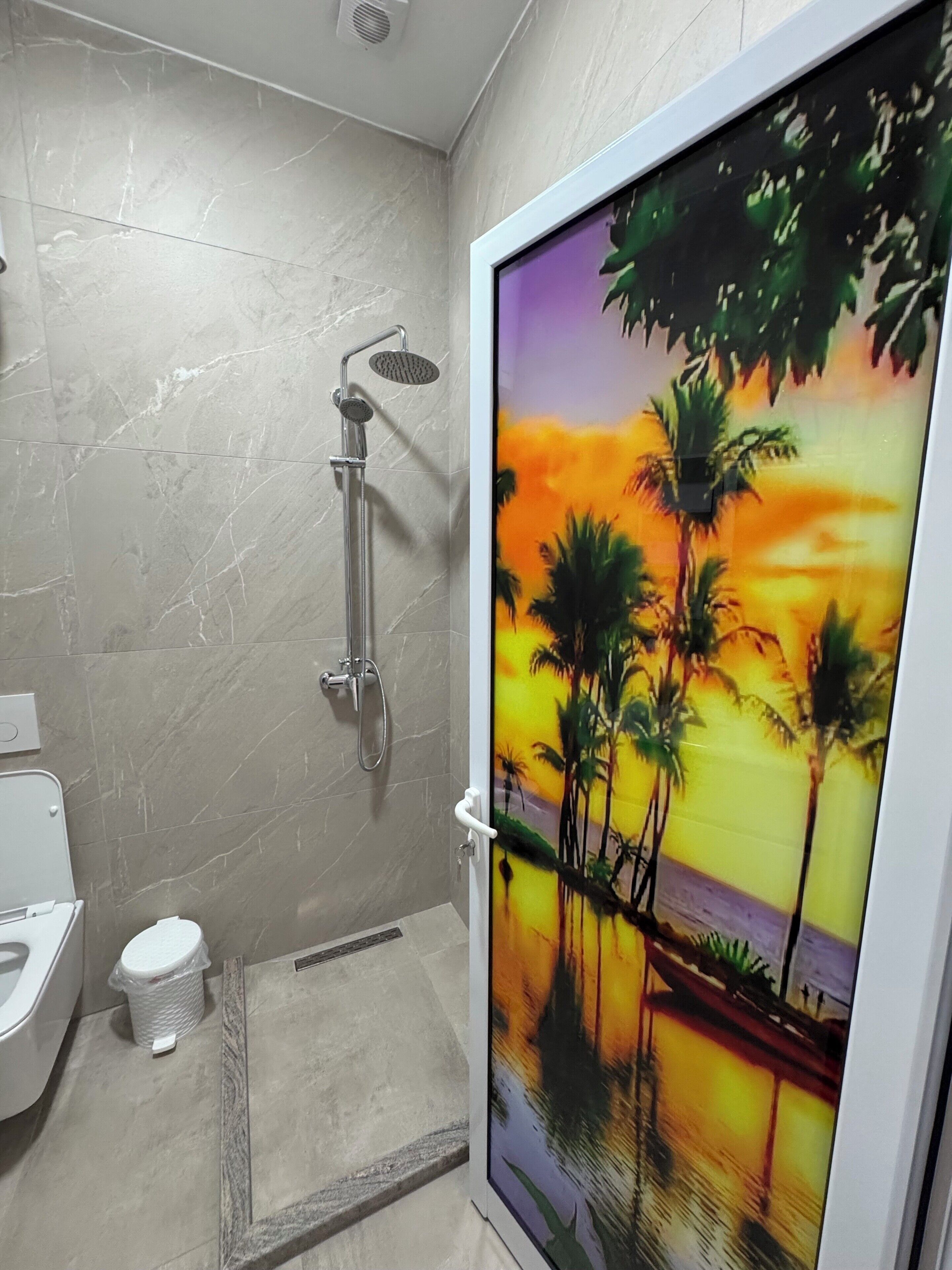 Baño con ducha, inodoro y un mural de atardecer tropical en la pared.