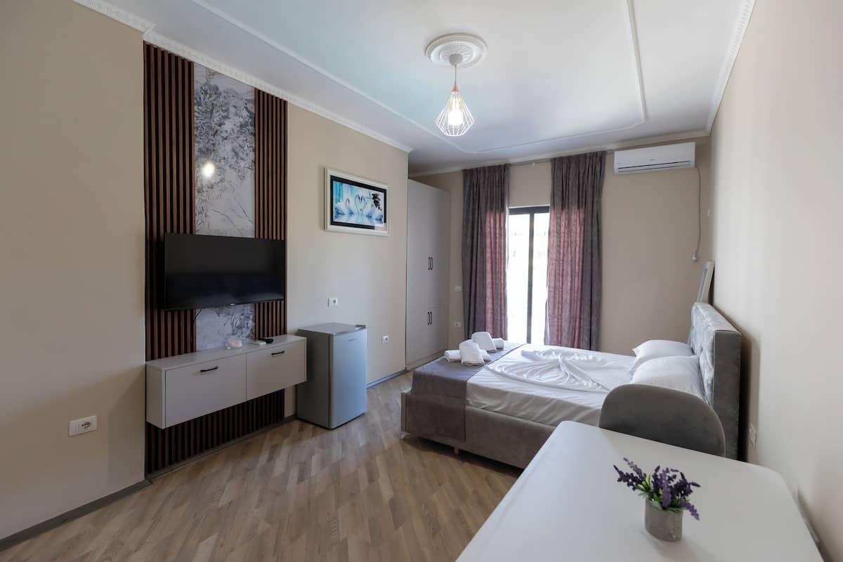 A hotel room with a bed, a desk, a TV, a small fridge, and a window with curtains.