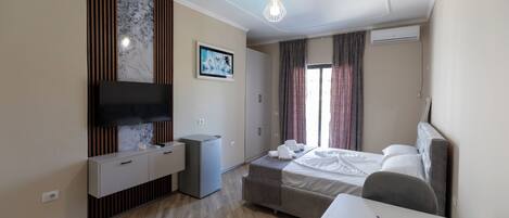 A hotel room with a bed, a desk, a TV, a small fridge, and a window with curtains.