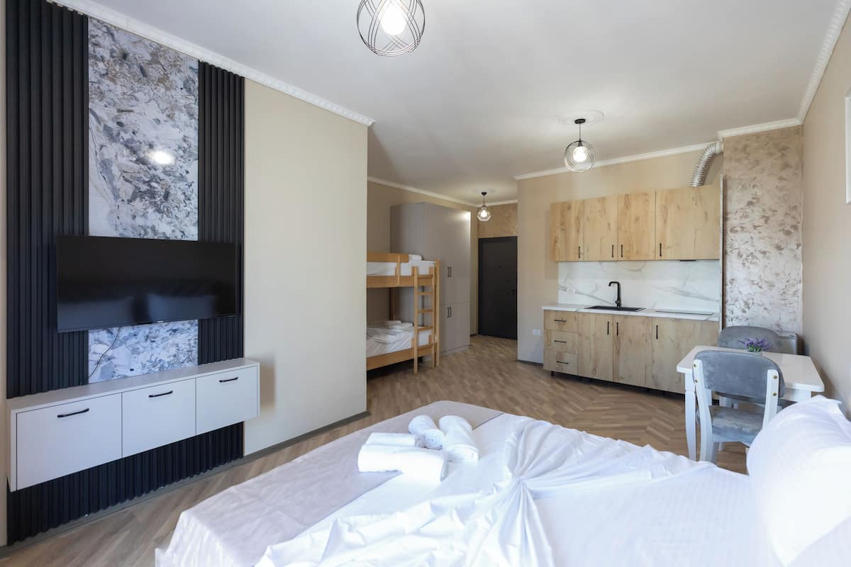 A modern hotel room with a bed, a TV, a kitchenette, and a bathroom.