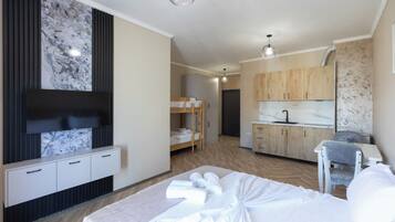 A modern hotel room with a bed, a TV, a kitchenette, and a bathroom.