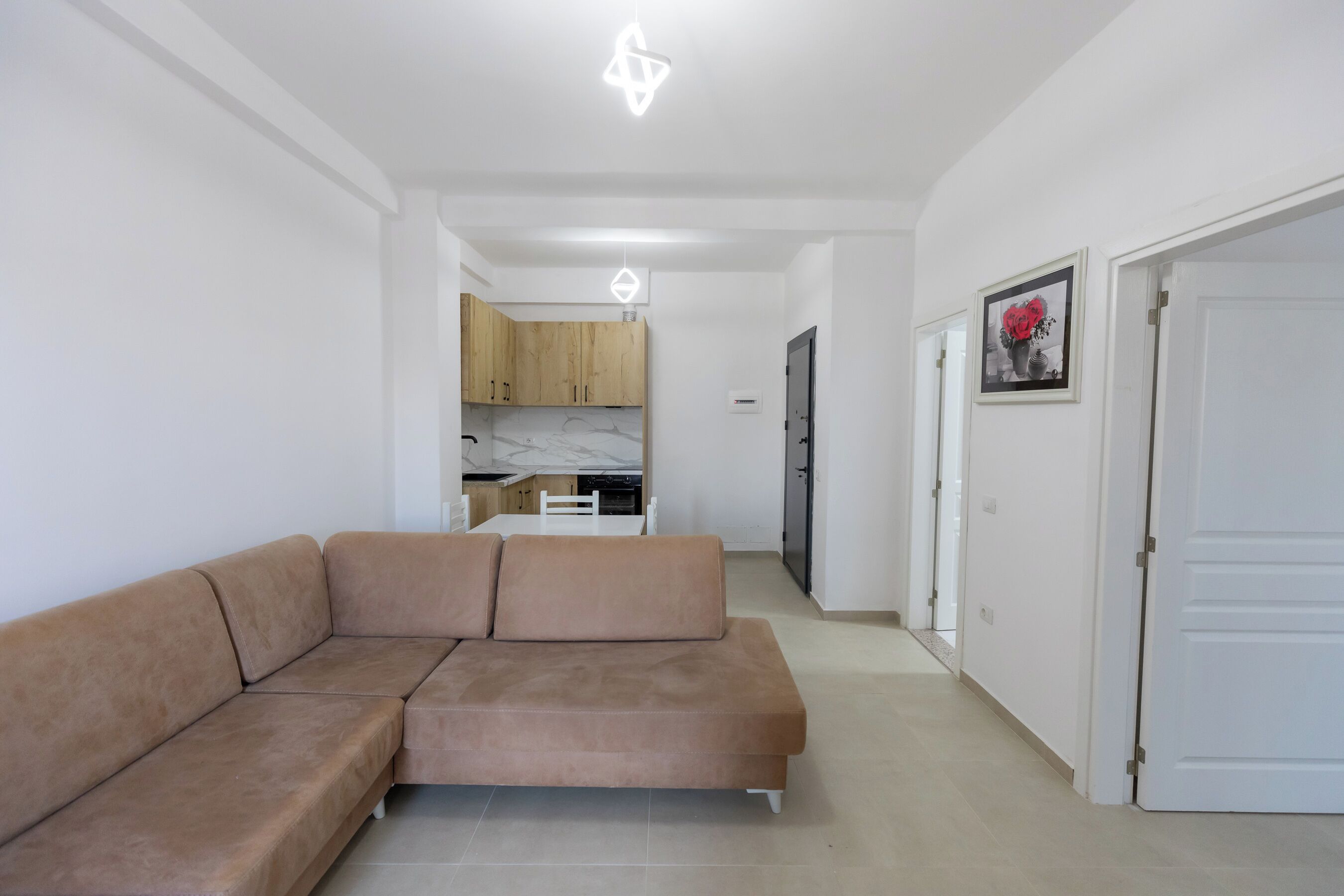 Un espace de vie moderne avec un canapé d’angle, une cuisine en arrière-plan et un couloir menant à une porte.