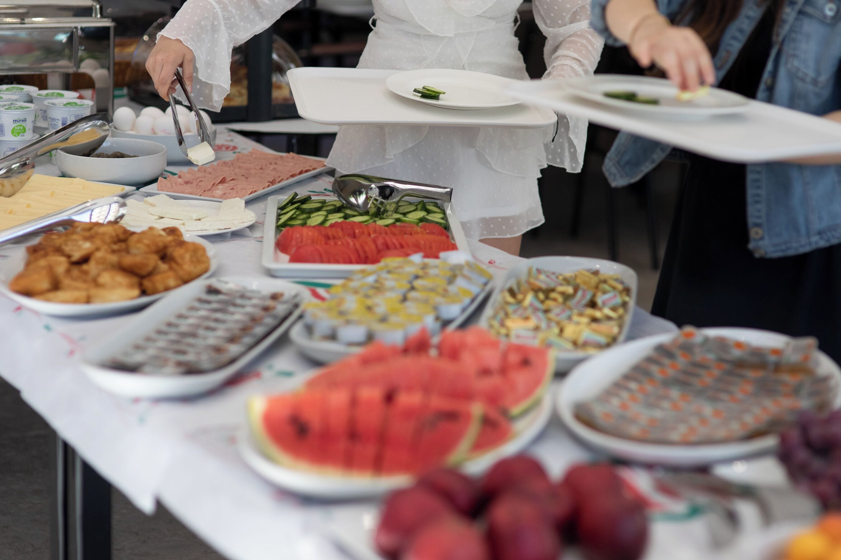 A buffet table with various food items including sliced watermelon, cheese, and other dishes.