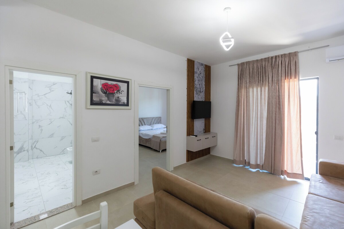 A modern bedroom with a bed, a TV mounted on the wall, and a bathroom with a marble shower.