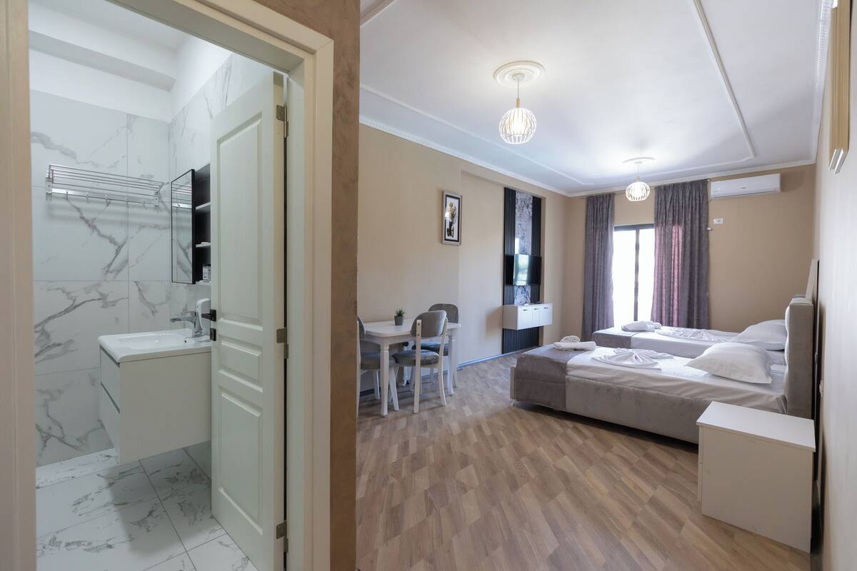 A modern hotel room with a bathroom, a dining area, and a bed.