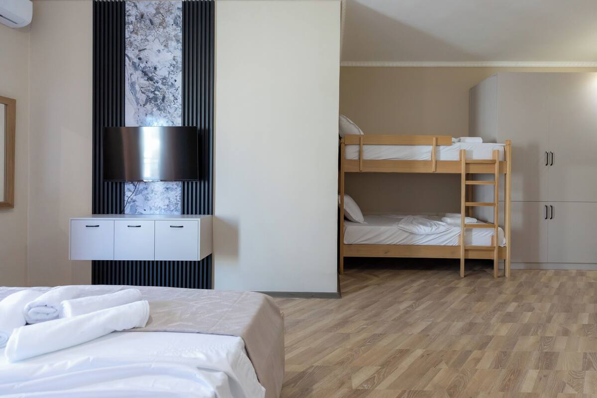 A hotel room with a bed, a TV mounted on a wall, a bunk bed, and a wardrobe.