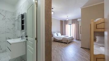 A hotel room with a marble bathroom, a wooden floor, a bed with white bedding, and a ceiling light.
