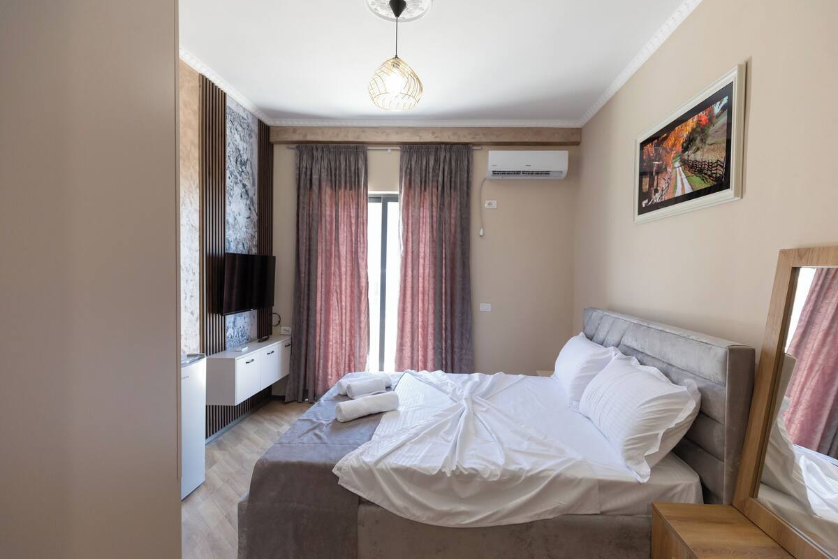 A modern hotel room with a bed, bedside table, and a TV on a white cabinet.