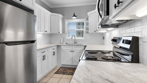 Une cuisine moderne avec des meubles blancs, un réfrigérateur en acier inoxydable, une cuisinière et un four à micro-ondes.