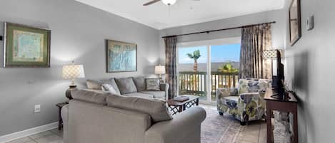 A living room with a sofa, armchairs, a ceiling fan, and a view of the outdoors.