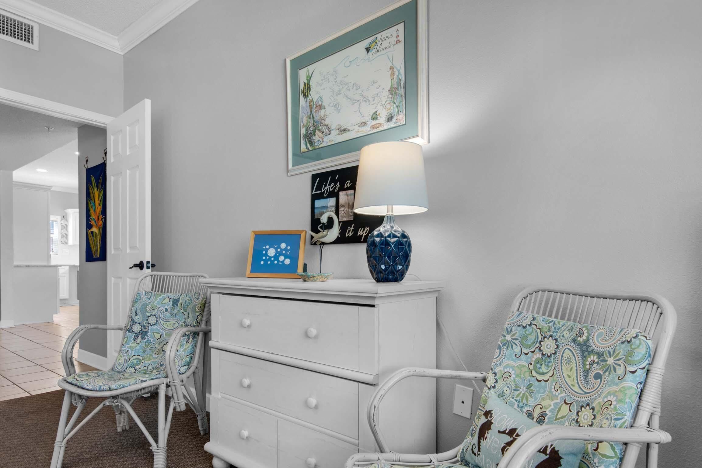 A room with two wicker chairs, a white dresser, and a wall-mounted lamp.