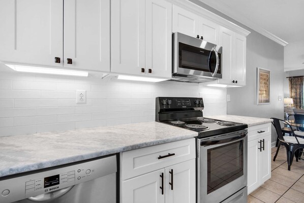 A modern kitchen with white cabinets, a Bosch dishwasher, a stainless steel microwave, and a gas stove. - Villas on the Gulf Unit J10 (Pensacola Beach)