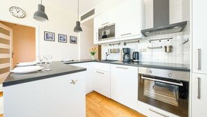 A modern kitchen with white cabinets, a black countertop, stainless steel appliances, and pendant lighting. - Apartamenty Sun & Snow Golden Tulip (Miedzyzdroje)
