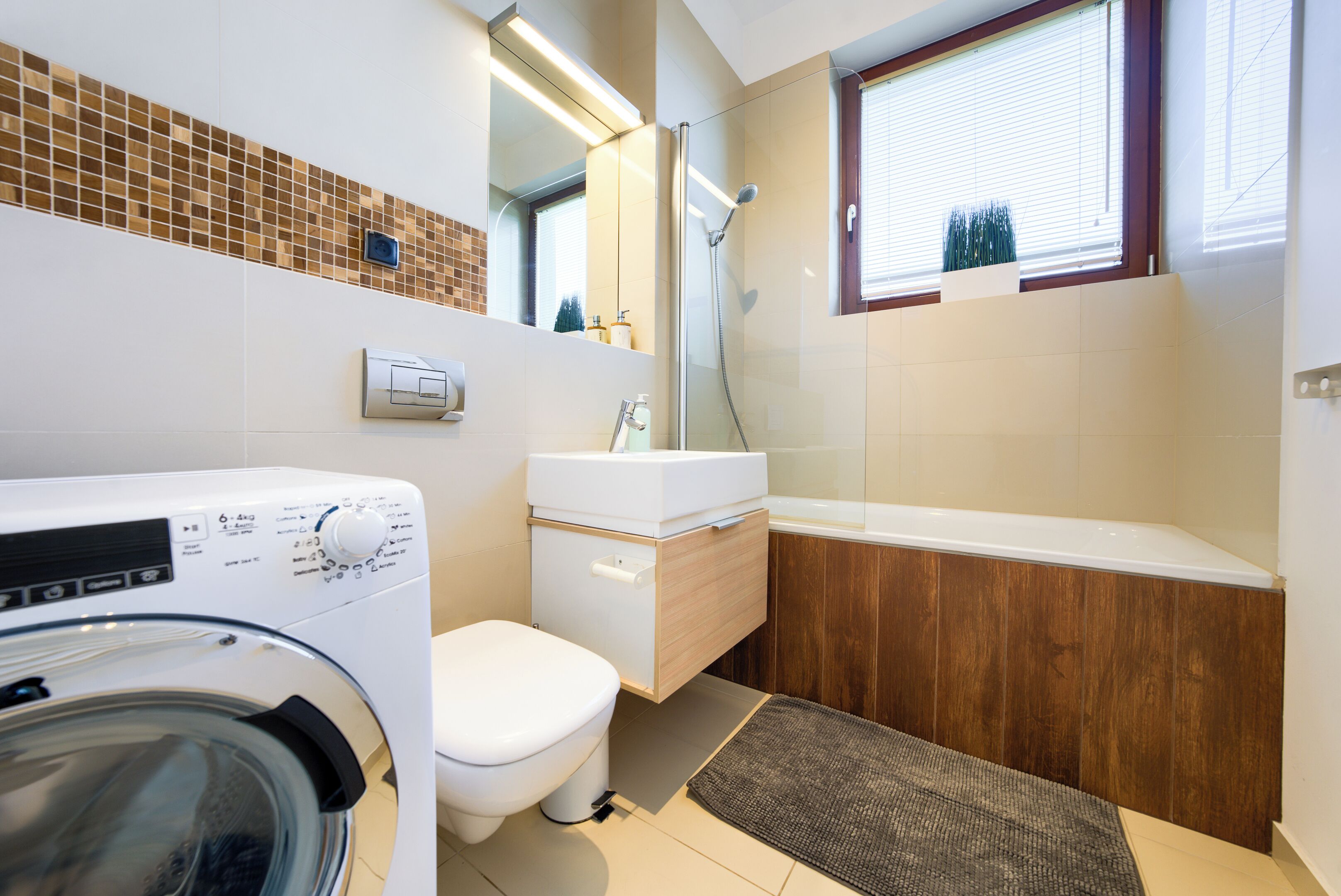 A modern bathroom with a washing machine, toilet, vanity, and bathtub.