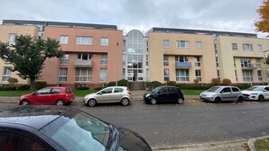 A row of multi-story residential buildings with a central entrance, parked cars, and a tree in the foreground. - Apartment Classic (Jülich)